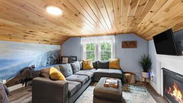 A cozy living room with a sectional sofa, a fireplace, a flat-screen TV, and a mural of a mountain landscape.