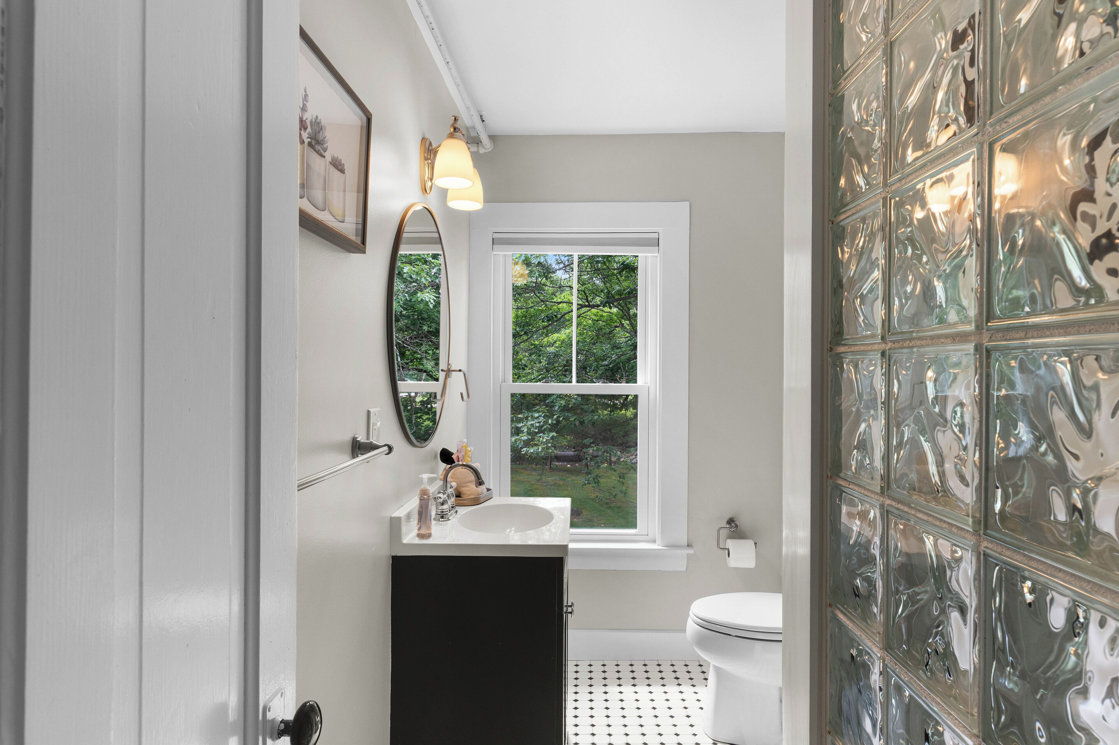 A bathroom with a white sink, a mirror, a window, and a toilet.