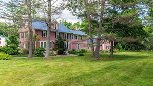 A large, two-story house with a red exterior and a blue roof, surrounded by a well-maintained lawn and several trees. - TuckAway Suites at East Branch (Intervale)