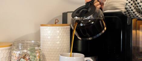 A coffee maker pouring coffee into a mug labeled "Tuckaway Suites at East Branch."