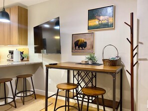 A kitchen with wooden cabinets, a flat-screen TV, a painting of a bison, and a wooden table with stools. - Center of Grand Lake- A Cozy Lakeside Suite- 7 Mins to RMNP (Grand Lake)