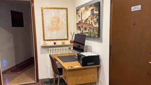 A hotel room with a wooden desk, a computer, a framed portrait, and a cityscape painting. - ARENA AROUND - IMPERIAL SUITE (Verona)