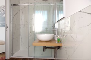 Un bagno moderno con cabina doccia in vetro, lavabo in marmo bianco e piano di appoggio in legno.