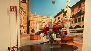 A table with a vase of flowers in front of a painting of a city square. - ARENA AROUND - IMPERIAL SUITE (Verona)