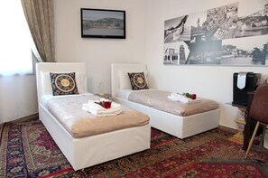 Camera d'albergo con due letti, un tappeto grande, una televisione e una parete con numerose fotografie in bianco e nero.