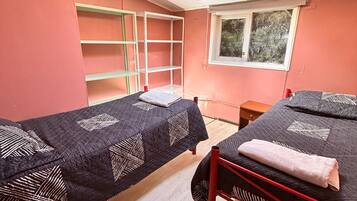 Une chambre de dortoir avec deux lits simples, une fenêtre, un ventilateur de plafond et une étagère.