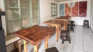 A dining area with wooden tables and stools, white tiled floor, and large windows with green frames. - Casa Piwke (Coyhaique)