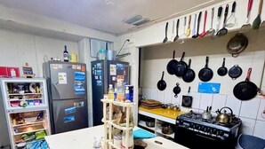 A kitchen with a central island, a refrigerator, a stove, and a variety of hanging pots and pans. - Casa Piwke (Coyhaique)
