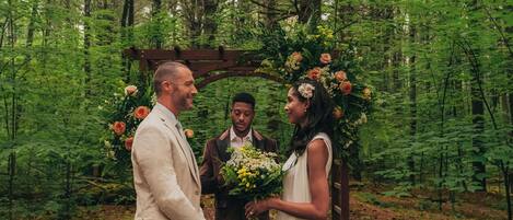 A forest setting with a wooden archway decorated with flowers.