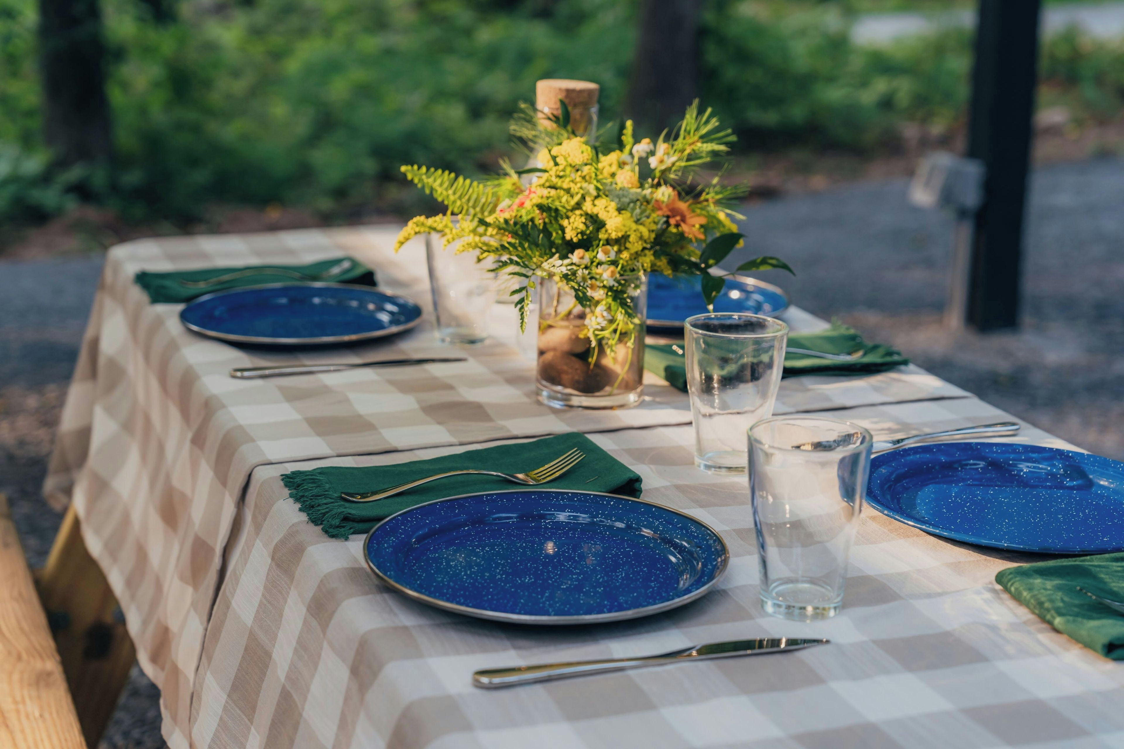 A table set with blue plates, a clear glass, and a vase with flowers.