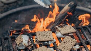 A grill with marshmallows and graham crackers being toasted over an open fire.
