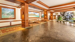 A spacious lobby with wooden beams, large windows with beach and waterfall views, and a stone floor.