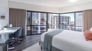 Habitación de hotel moderna con una cama grande, un escritorio y vistas de la ciudad a través de ventanales de piso a techo.