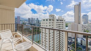 A balcony with white chairs and a table, overlooking a cityscape with tall buildings and a river. - 🍧 Summer Special - Royal Garden Waikiki - Ocean View - Resort Amenities 😎 (Honolulu)