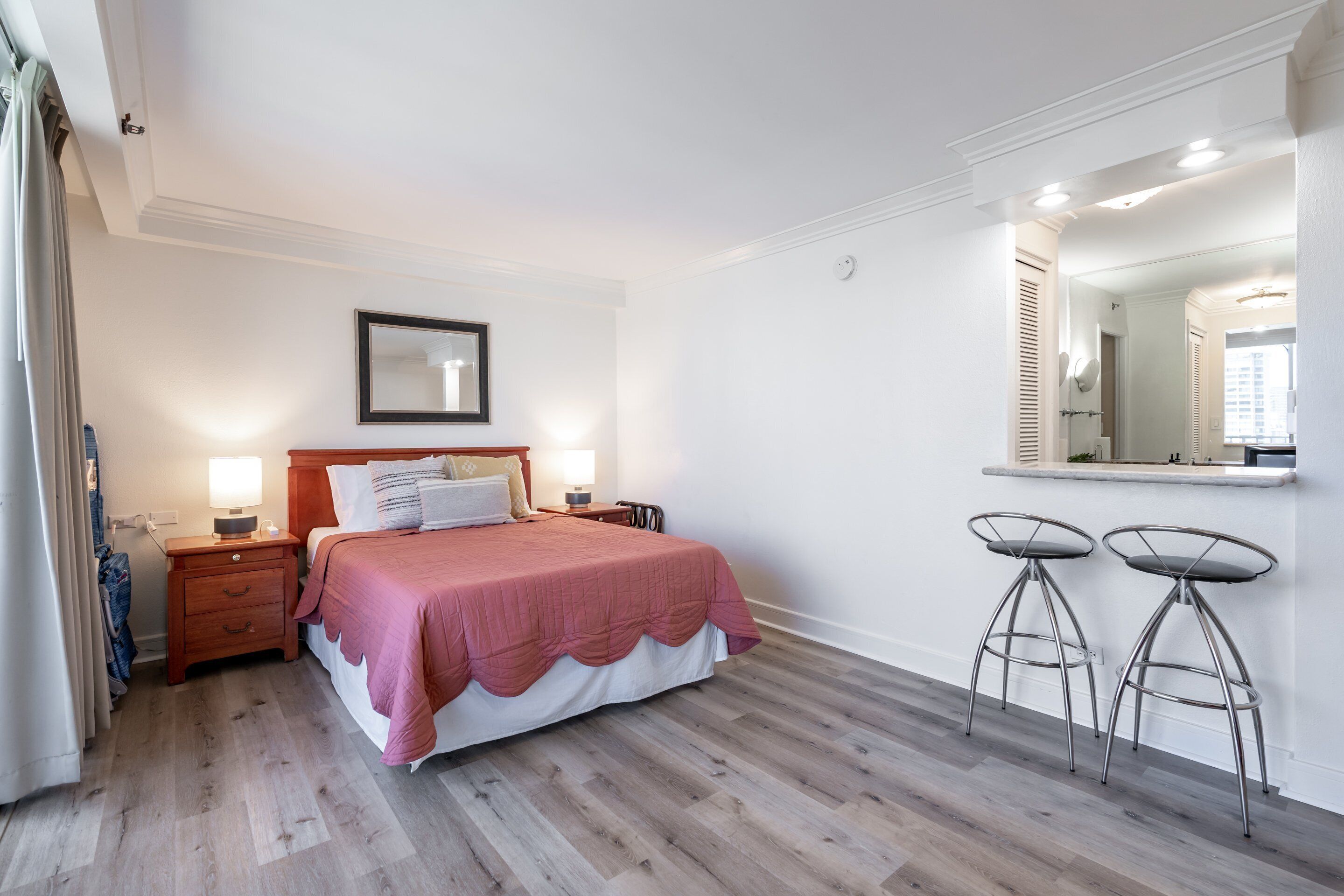 A bedroom with a bed, bedside tables, a mirror, and two bar stools.