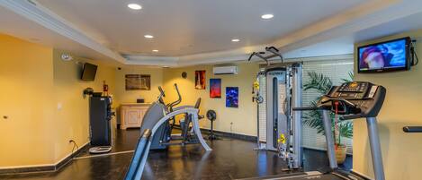 Une salle de sport équipée de machines de cardio, d’un tapis de course et d’un téléviseur fixé au mur.