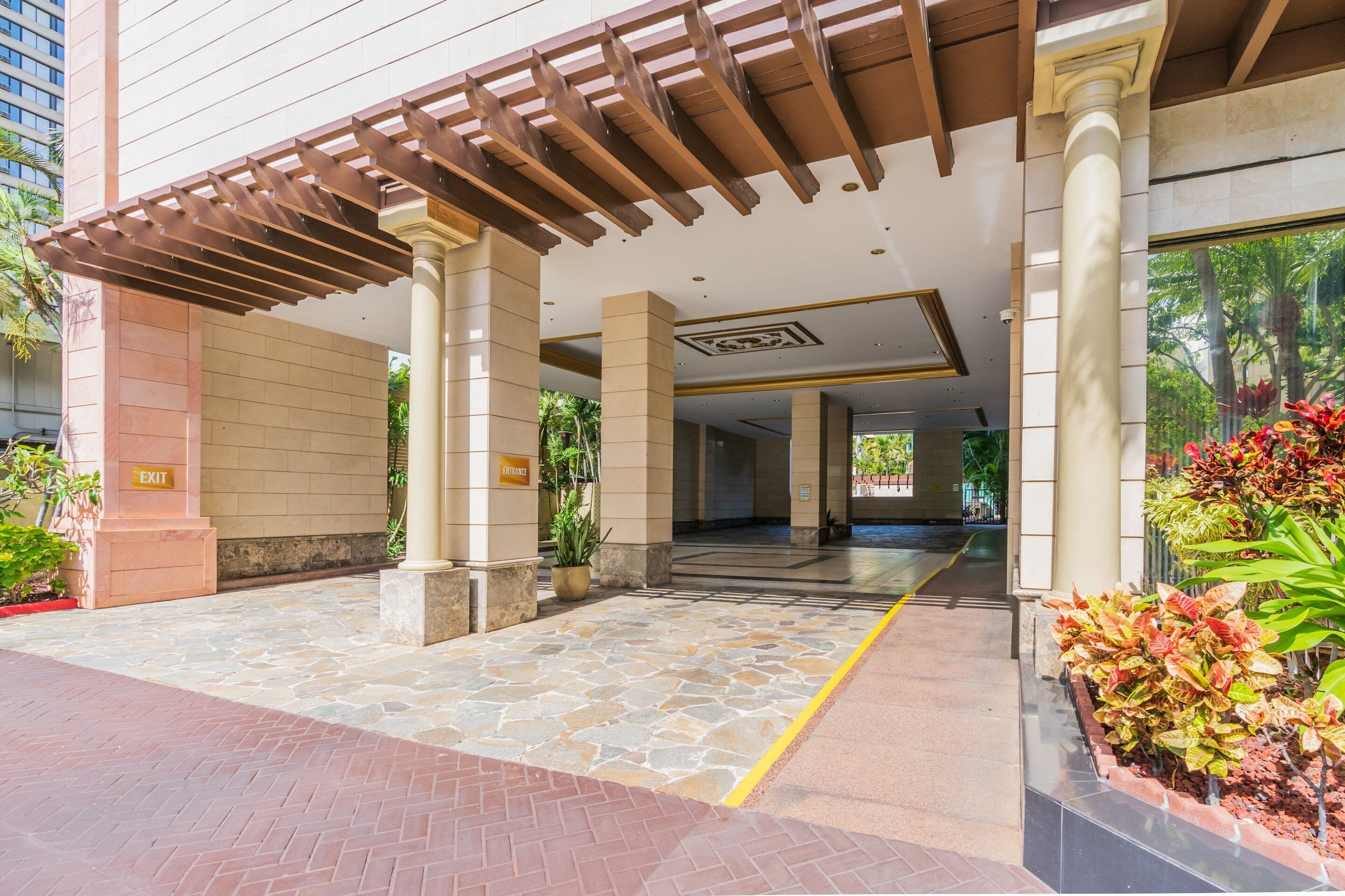 A covered entrance with stone flooring, columns, and a pergola.