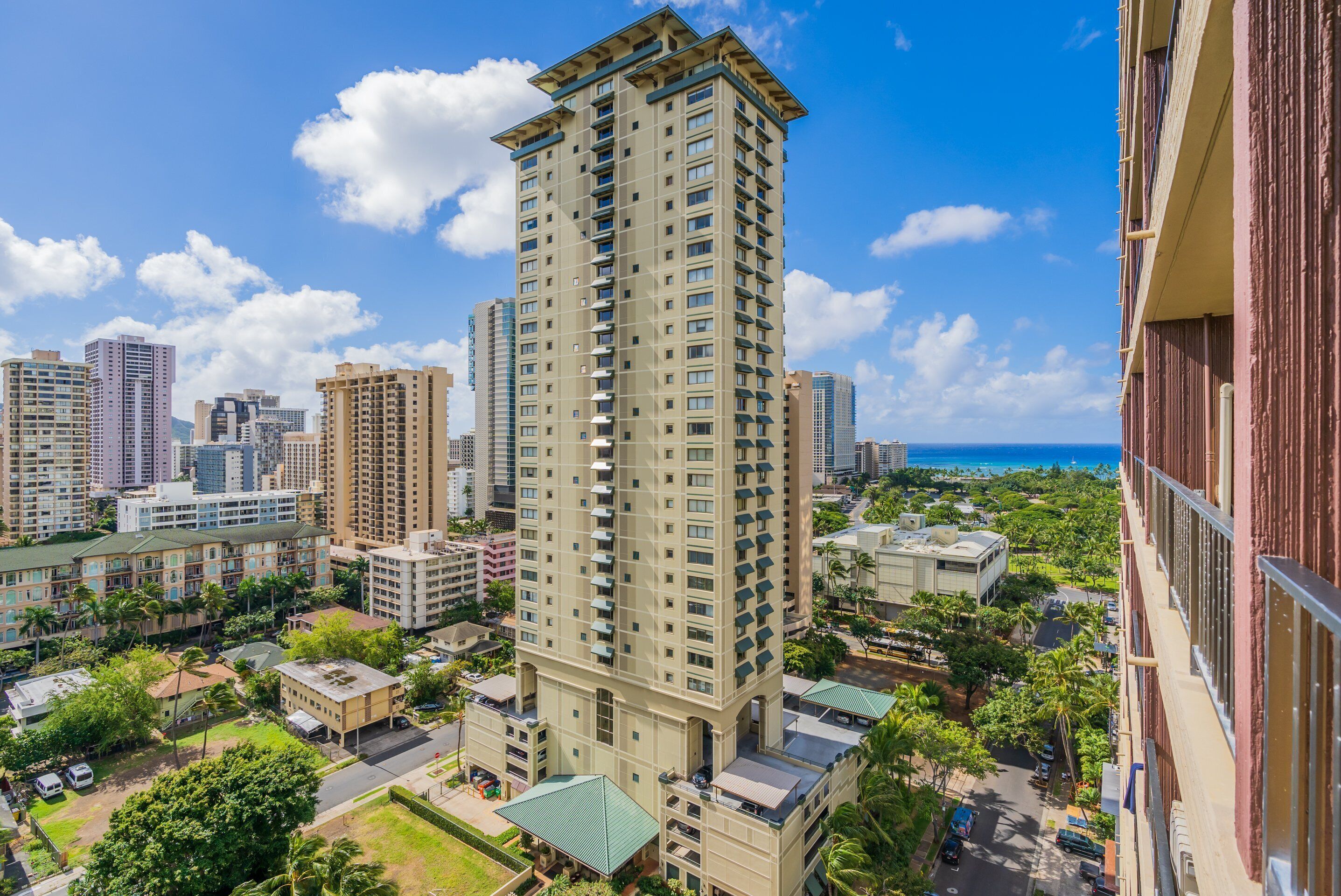 A high-rise building with multiple balconies, surrounded by other buildings and greenery.