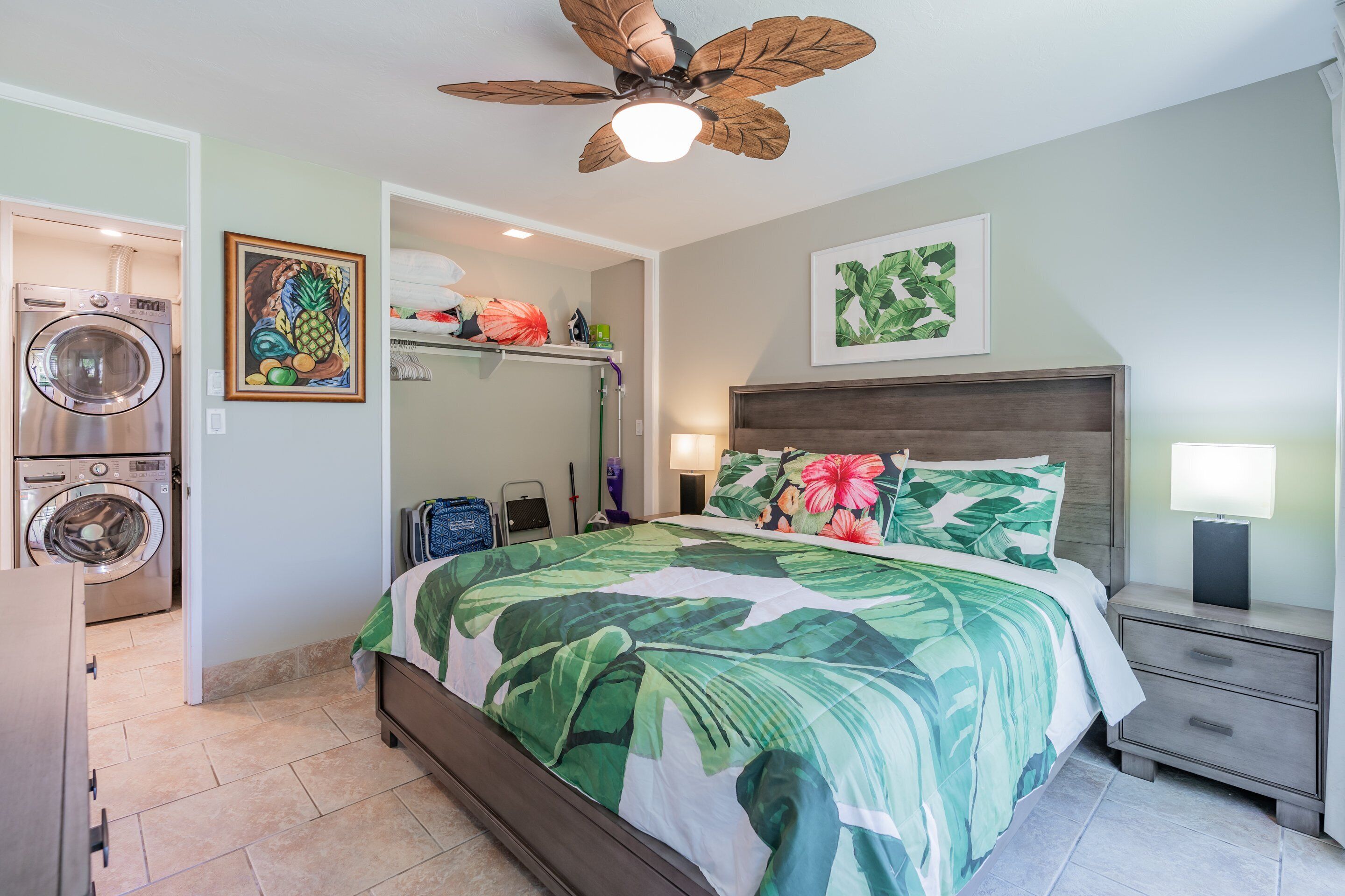 A bedroom with a bed, a ceiling fan, a nightstand, a dresser, a washing machine, and a laundry basket.