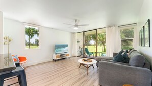 Amplia sala de estar con un sofá gris, una mesa de centro redonda y un televisor sobre un mueble blanco.