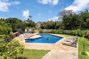Un jardin avec une piscine, des chaises longues et une maison en arrière-plan.