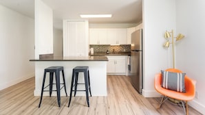 Una cocina moderna con armarios blancos, una isla central con taburetes, un refrigerador de acero inoxidable y una lámpara de pie.