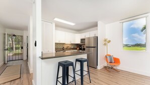 Una cocina moderna con armarios blancos, un refrigerador de acero inoxidable y un taburete de bar.