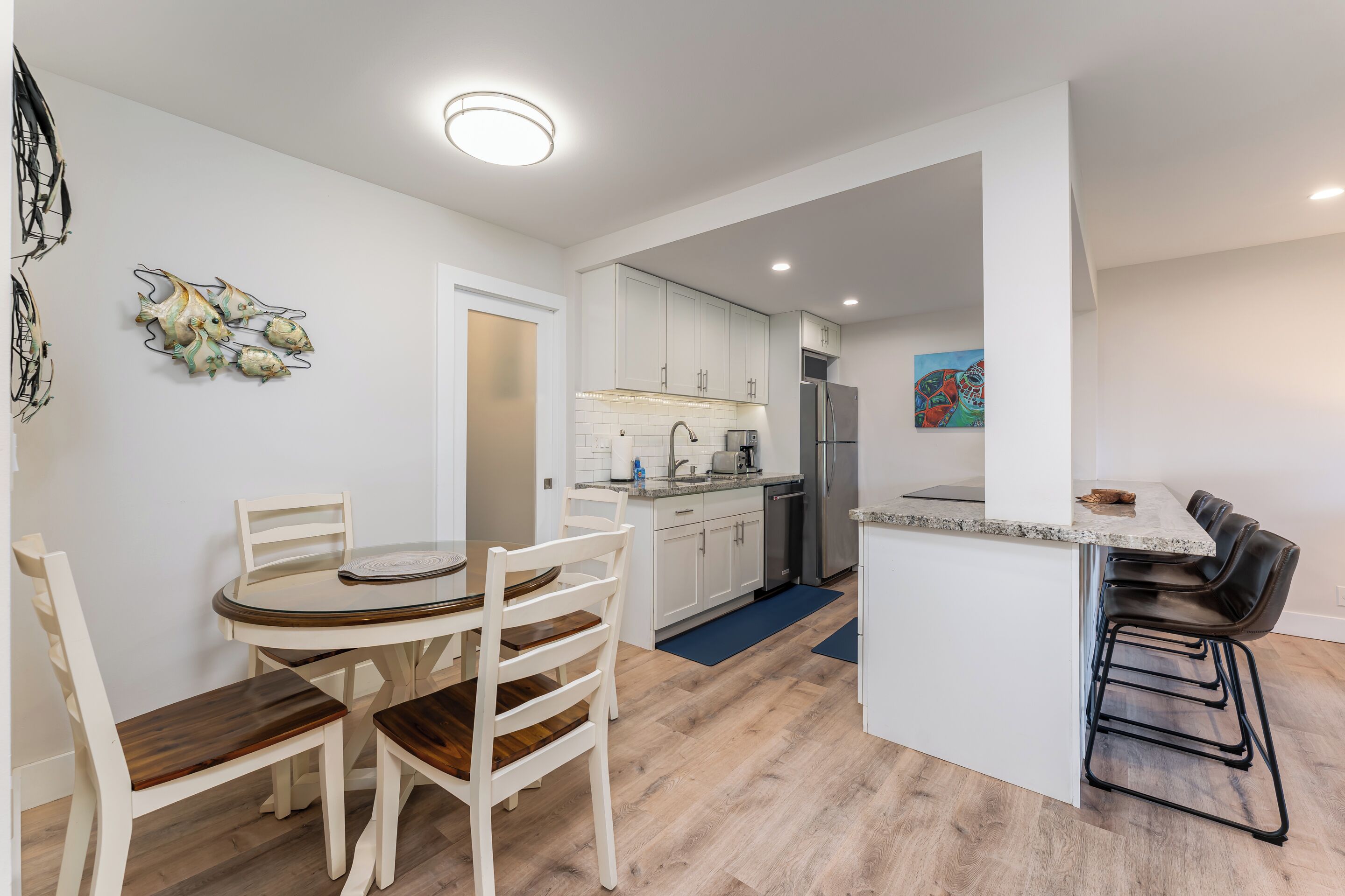 A modern kitchen with white cabinets, a stainless steel refrigerator, and a dining area with a round table and chairs.