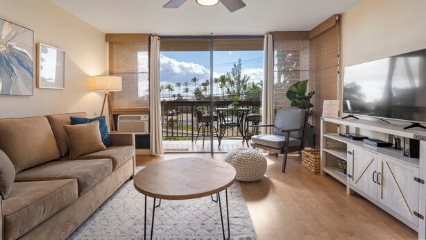 Un salon comprenant un canapé, une table basse, un téléviseur et un balcon aménagé avec du mobilier d’extérieur.