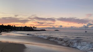 Une plage avec des vagues, une île au loin et des bâtiments qui bordent le rivage.