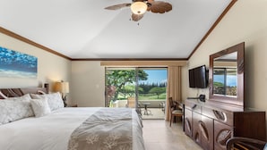 Ett hotellrum med en stor säng, en takfläkt, en TV, en matplats med bord och stolar samt utsikt över en golfbana.