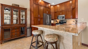 Ett kök med träskåp, ett kylskåp i rostfritt stål, en mikrovågsugn och en bänkskiva i granit.
