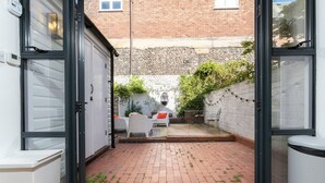 Un patio con suelo de ladrillo, mobiliario blanco y pared de ladrillo.