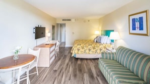 Une chambre d’hôtel comprenant un lit, un canapé, un bureau avec une chaise, une petite table et un téléviseur fixé au mur.
