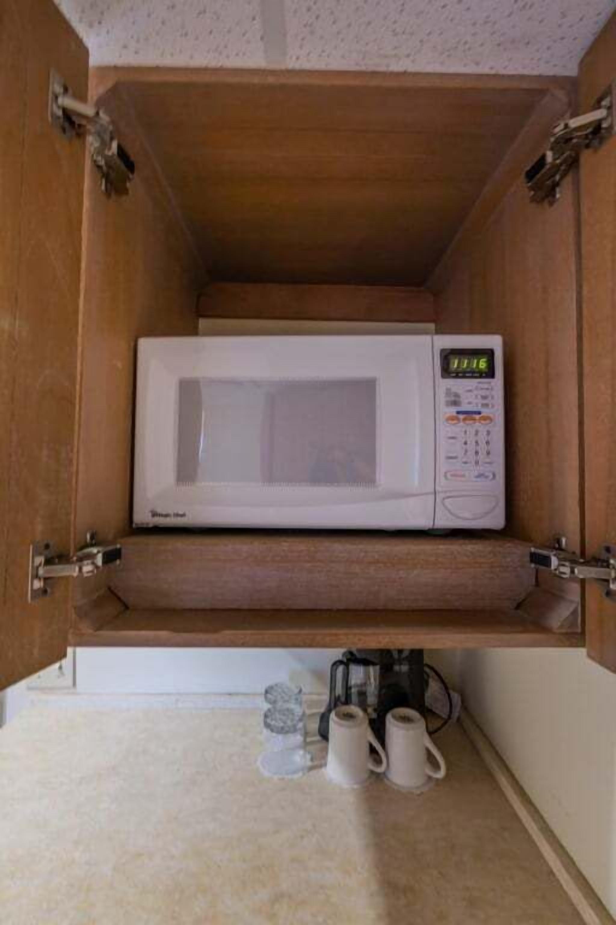 Un microondas dentro de un mueble de madera, con una cafetera y dos tazas debajo.