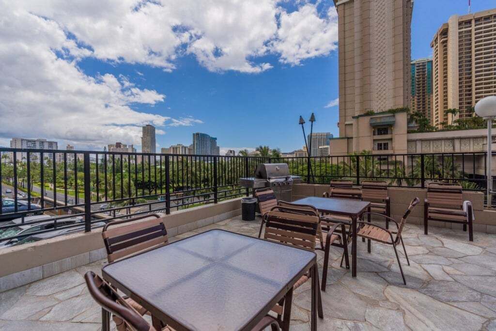 An outdoor patio with tables and chairs, a grill, and a view of the city skyline.