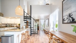 A modern kitchen with a central island, wooden bar stools, and a staircase leading to an upper level. - 😎🍧Summer Special - The Drifter - North Shore Loft - Relaxed Luxury ☀️🏄‍♀️ (Kahuku)