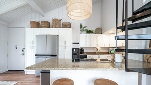 A modern kitchen with white cabinets, a granite island, wooden stools, and a hanging light fixture. - 😎🍧Summer Special - The Drifter - North Shore Loft - Relaxed Luxury ☀️🏄‍♀️ (Kahuku)