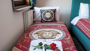 Un lit bien fait, recouvert d’une couvre-lit aux motifs rouges et dorés, agrémenté d’un coussin décoratif et d’une serviette ornée d’une rose rouge.