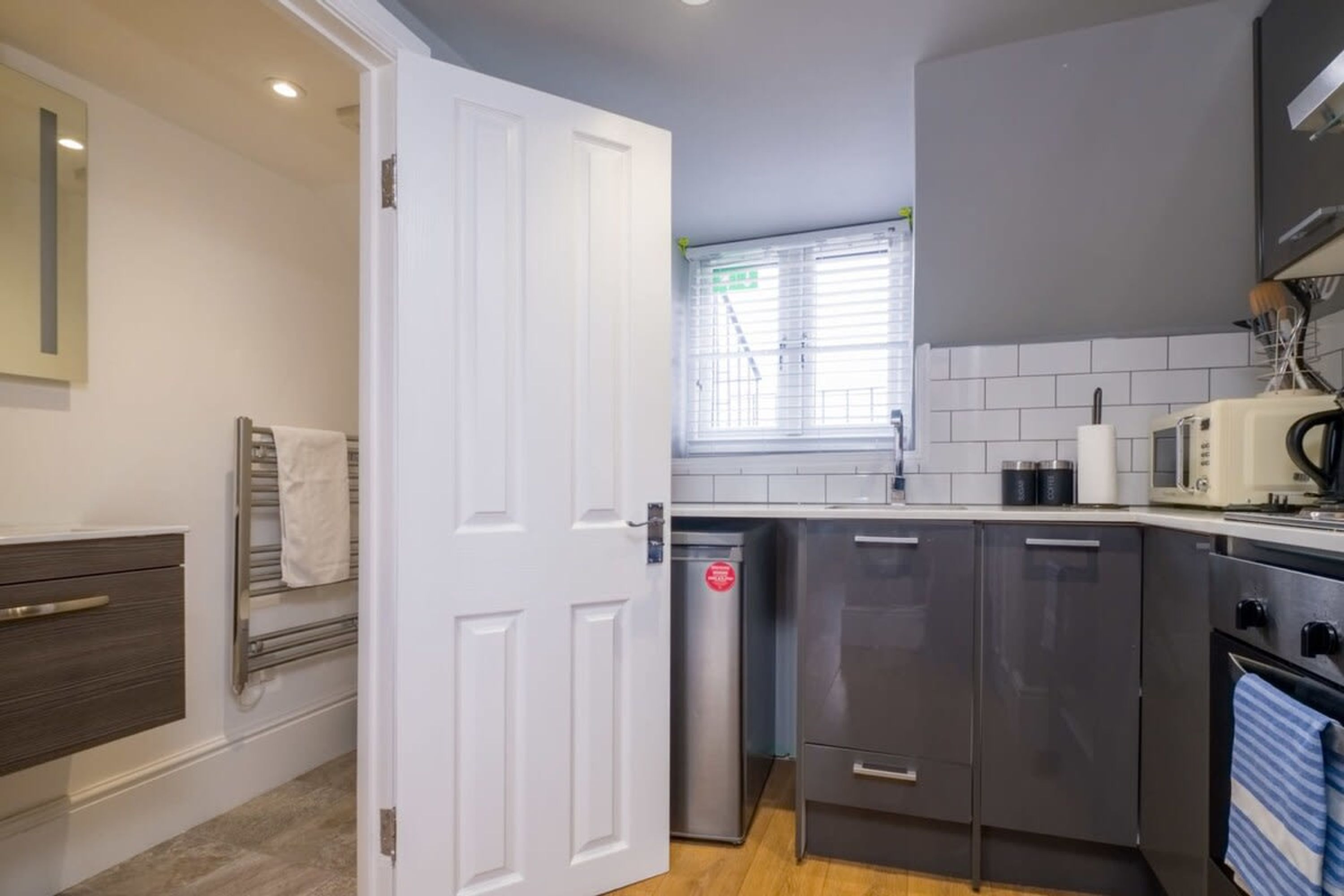A compact kitchen with a white door, stainless steel appliances, and a tiled backsplash.