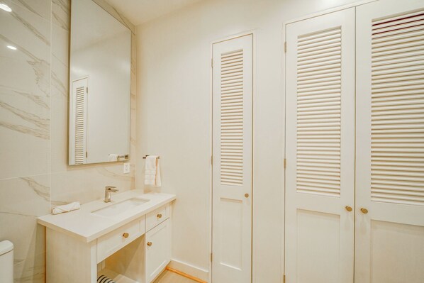 A bathroom with a white vanity, a mirror, and a toilet. - Modern Island Living – 2-Bed, 2-Bath Beachfront Condo at Watercolors Roatán E4 (Roatán)