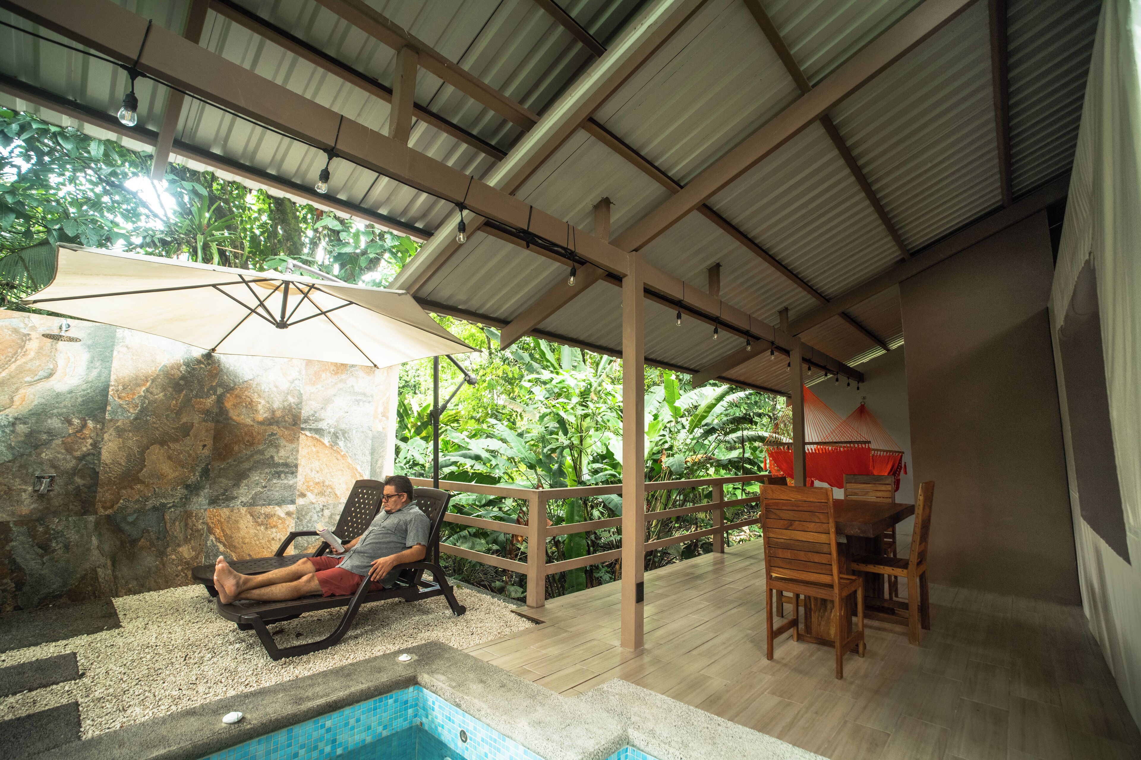 A covered outdoor area with a pool, lounge chairs, and a dining table.