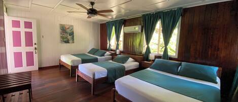 A room with three beds, a ceiling fan, a door with pink panels, and a window with curtains.