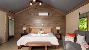 A bedroom with a wooden ceiling, a bed with a heart-shaped decoration, two bedside tables with lamps, a bench, and a grey sofa with patterned cushions. - Valverde Glamping & Ecolodge (Colorado)