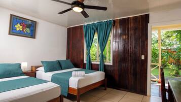 Habitación de hotel con dos camas, ventilador de techo, ventana con cortinas y puerta que da a un espacio exterior.