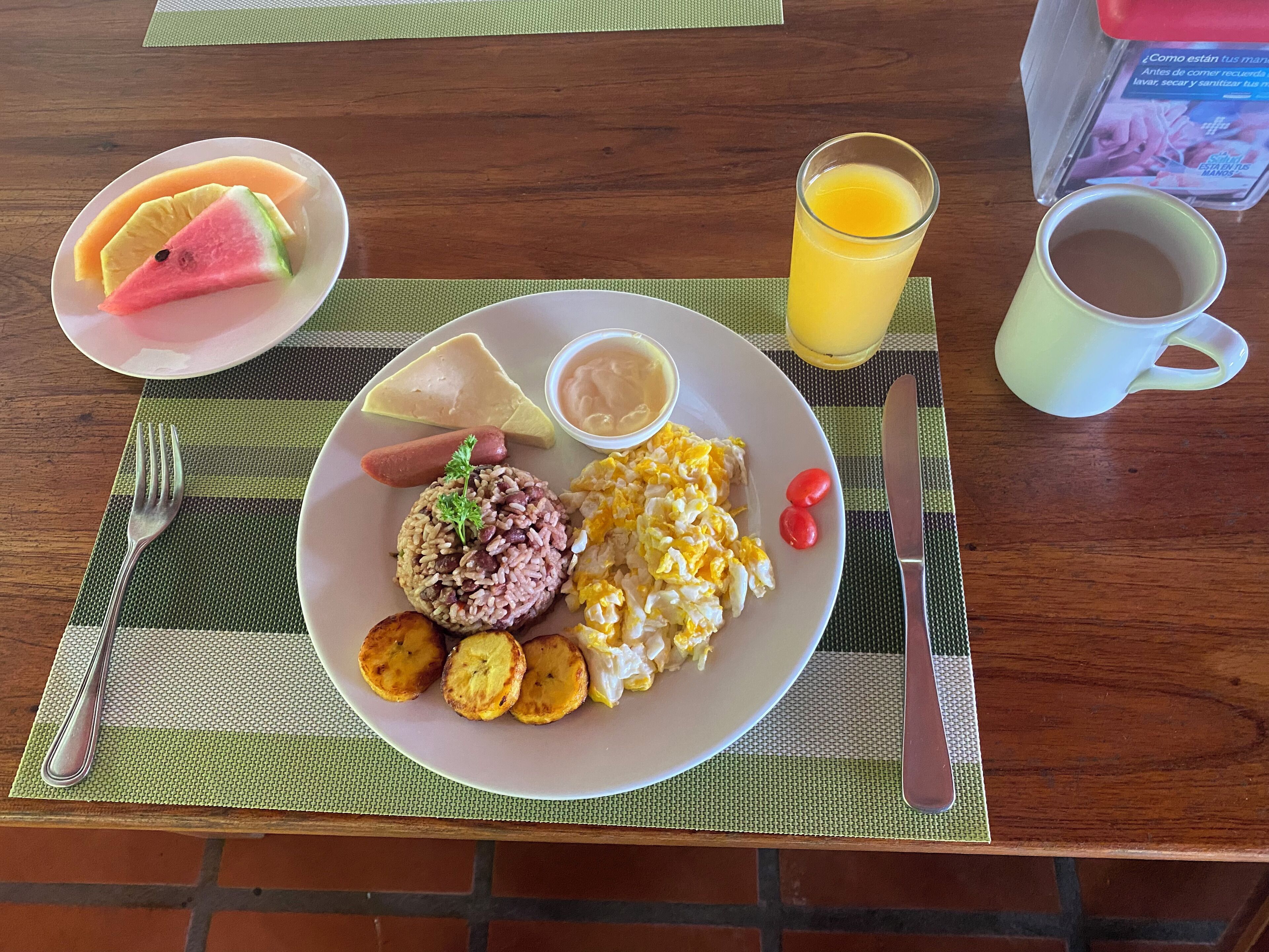 A breakfast plate with rice, eggs, tomatoes, and a slice of watermelon on a placemat.