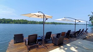 A wooden deck with outdoor seating and umbrellas overlooking a lake. - Valverde Glamping & Ecolodge (Colorado)