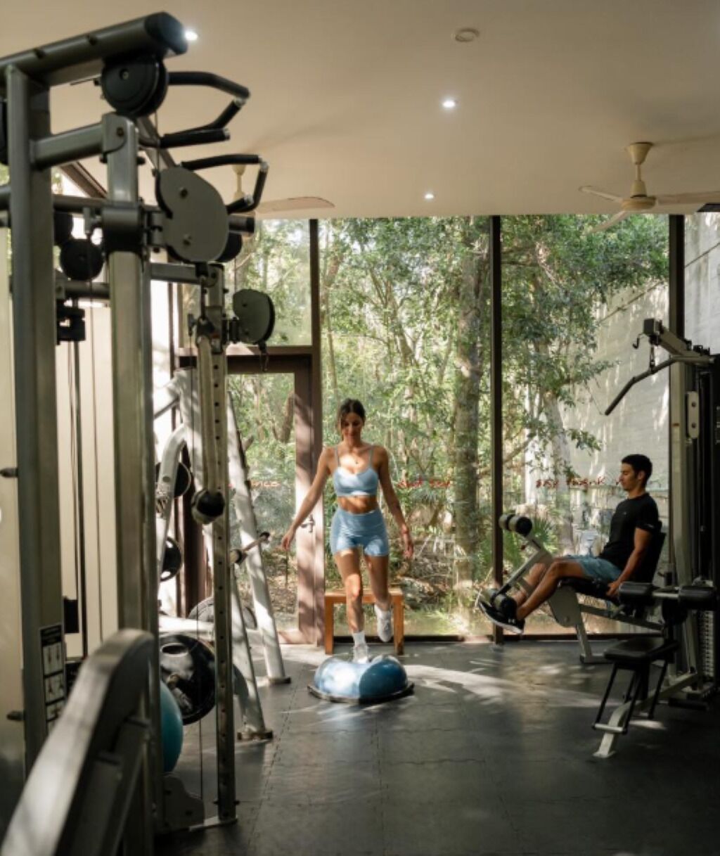 A gym with exercise equipment, large windows, and a ceiling fan.