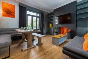 A modern living room with a wooden floor, grey sofa, wooden coffee table, and a TV mounted on the wall. - Host Stay Queens Maisonette (Brighton)