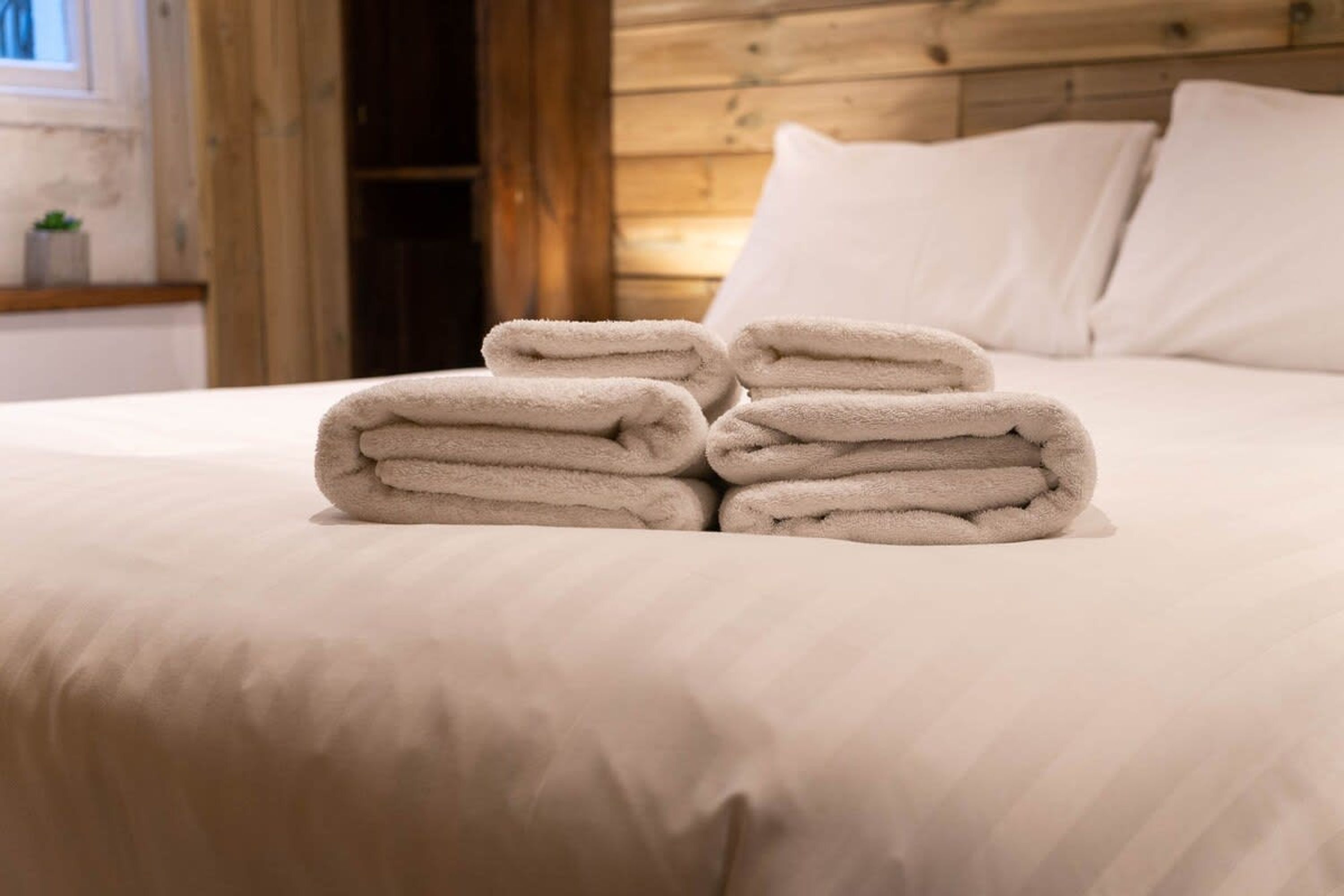 A neatly made bed with folded white towels in front of it.